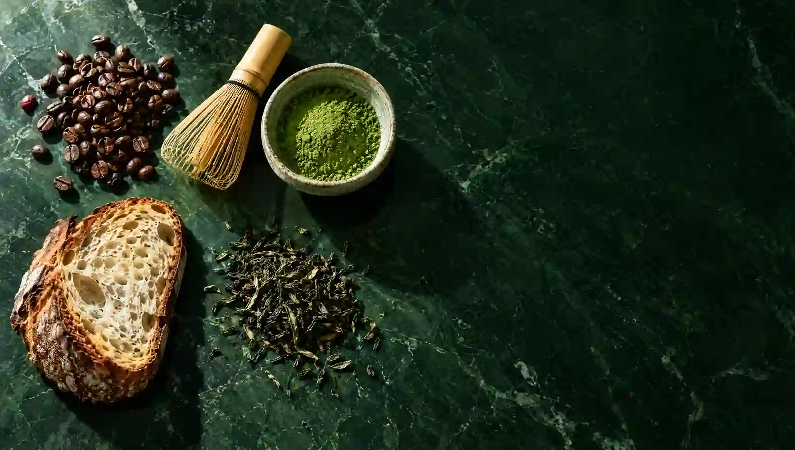 Coffee beans, matcha whisk, loose tea and sourdough bread on a green marble counter